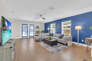Un soggiorno spazioso con una grande TV a schermo piatto, una ventola a soffitto e una parete decorata in blu.