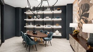 Un espace repas moderne avec une table ronde, des chaises bleues et un mur foncé agrémenté d’étagères.