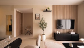 A modern living room with a flat-screen TV, a potted plant, a dining area with a glass table, and a sofa. - Maison De Gu Co Giang Apartment (Ho Chi Minh City)