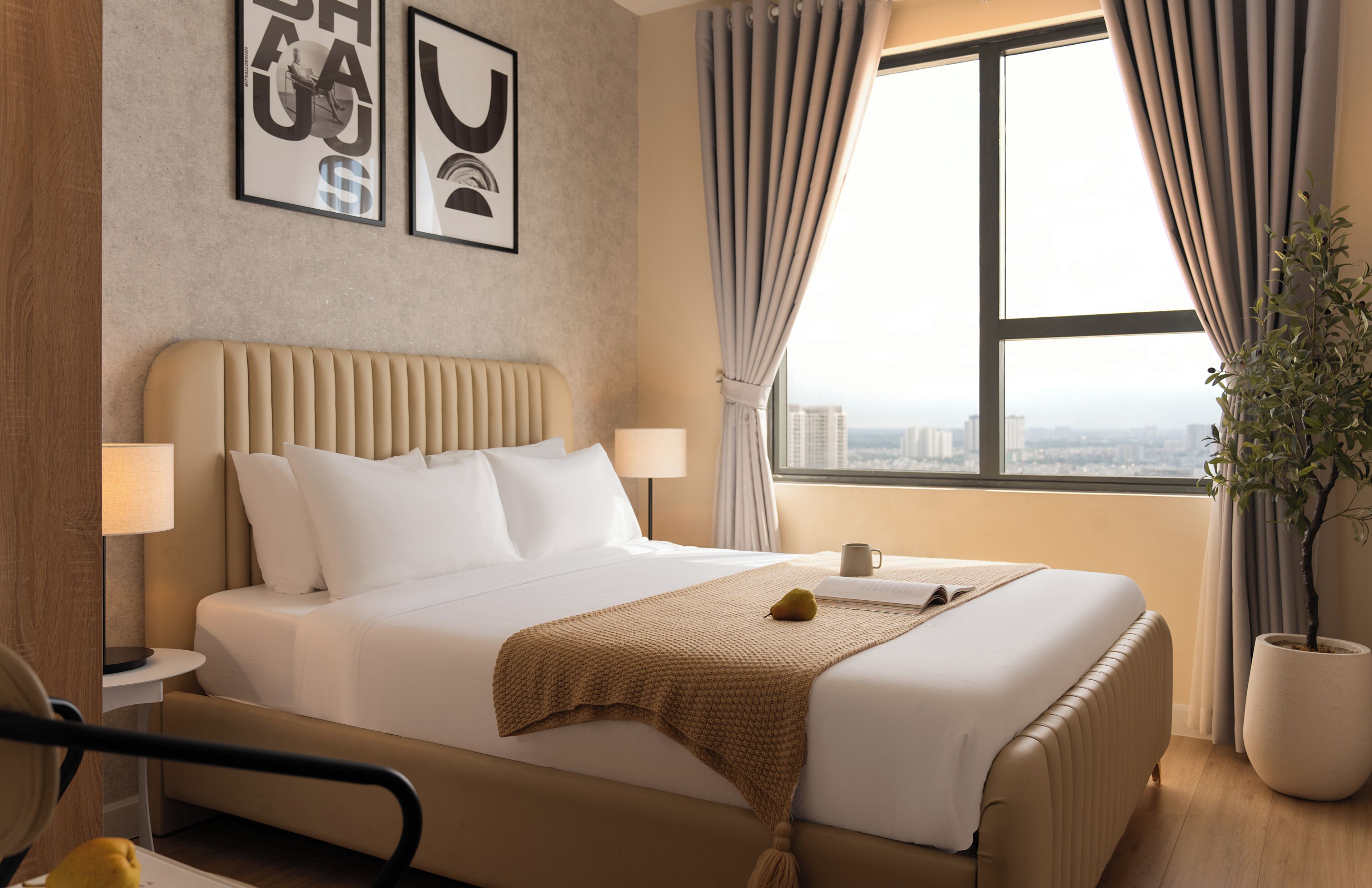 Une chambre d’hôtel avec un grand lit, une table de chevet, une lampe, une fenêtre avec des rideaux et une plante en pot.