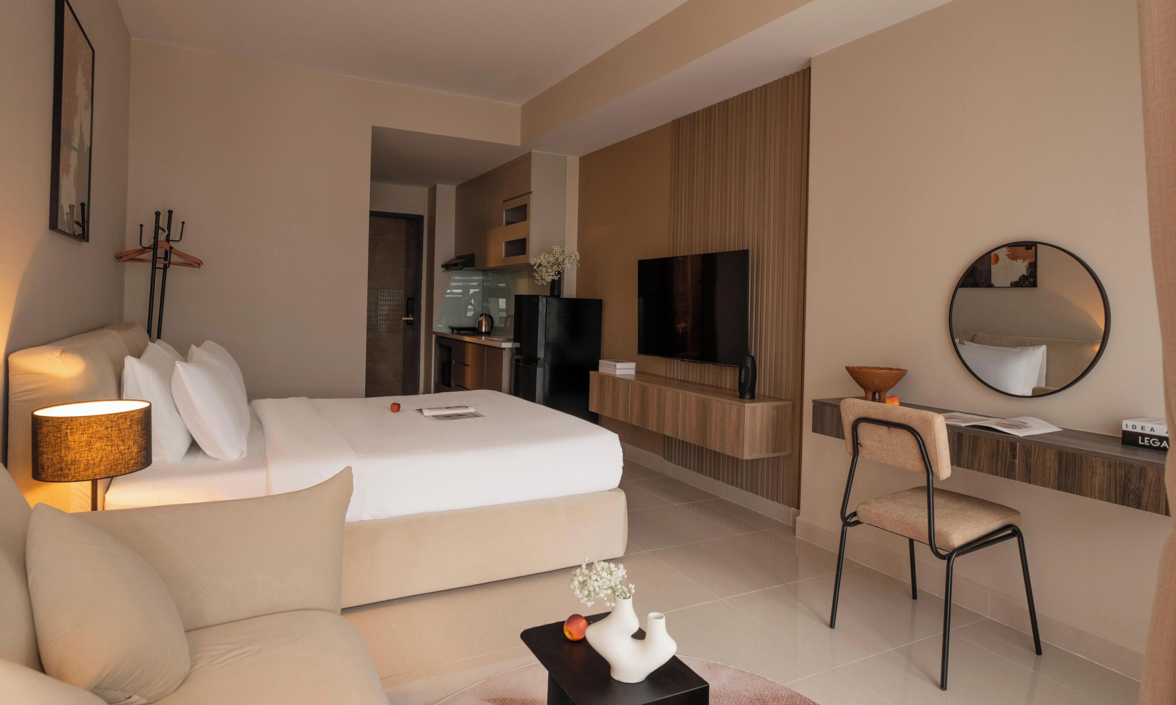 A hotel room with a bed, a sofa, a desk with a chair, a television, and a mirror.