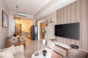 A modern living room with a flat-screen TV, a dining area with a table and chairs, and a kitchen in the background. - Maison De Gu Co Giang Apartment (Ho Chi Minh City)