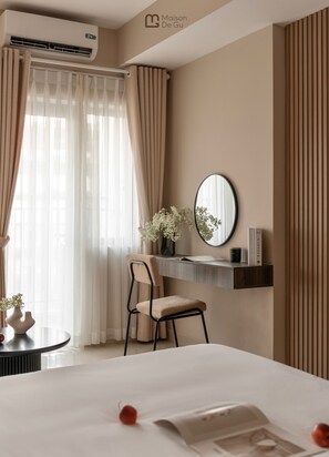 A hotel room with a bed, a desk with a chair, a mirror, a vase with flowers, and a book titled 'KINFOLK'. - Maison De Gu Co Giang Apartment (Ho Chi Minh City)
