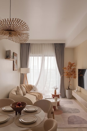 A modern living room with a dining area, featuring a sofa, dining table, and a large window with curtains. - Maison De Gu Co Giang Apartment (Ho Chi Minh City)