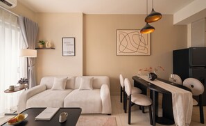 A modern living room with a sofa, dining table, chairs, and a black refrigerator. - Maison De Gu Co Giang Apartment (Ho Chi Minh City)