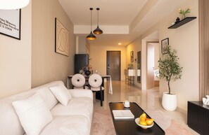 A modern living room with a sofa, a dining area with a table and chairs, a potted plant, and a coffee table with fruits. - Maison De Gu Co Giang Apartment (Ho Chi Minh City)