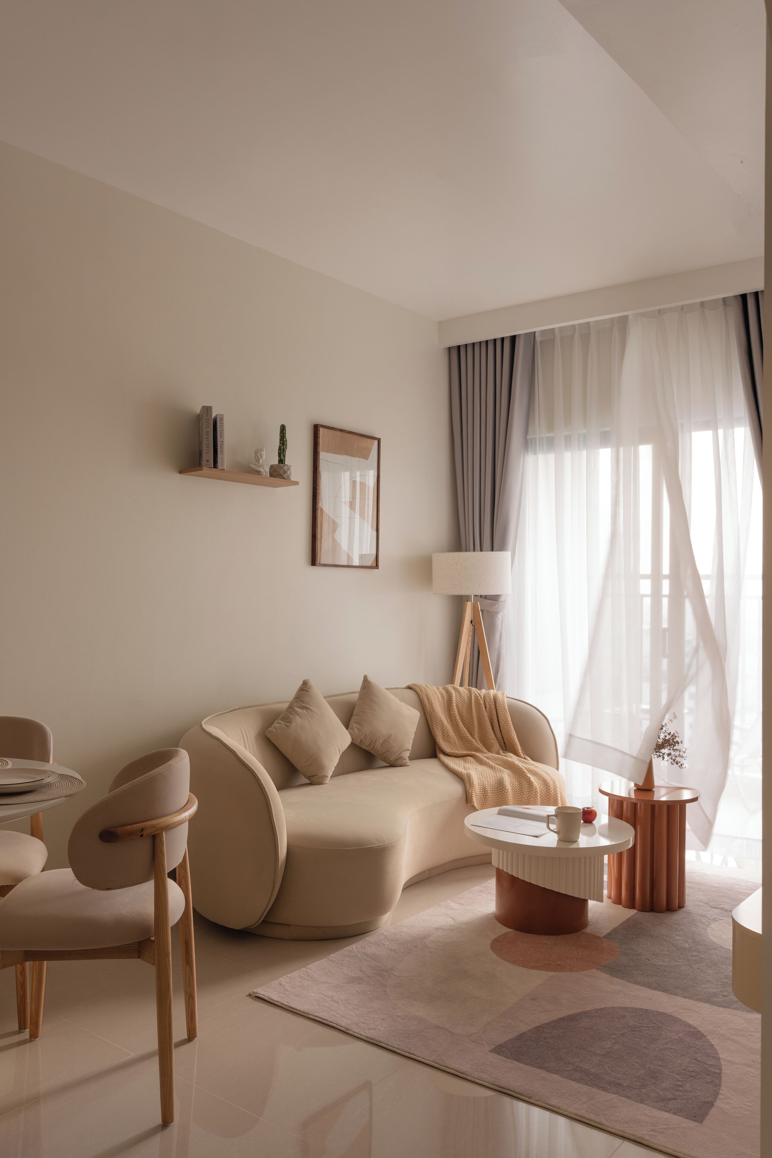 Un salon moderne avec un canapé, une table basse et des fauteuils. On y trouve une lampe, un tableau et une fenêtre avec des rideaux.