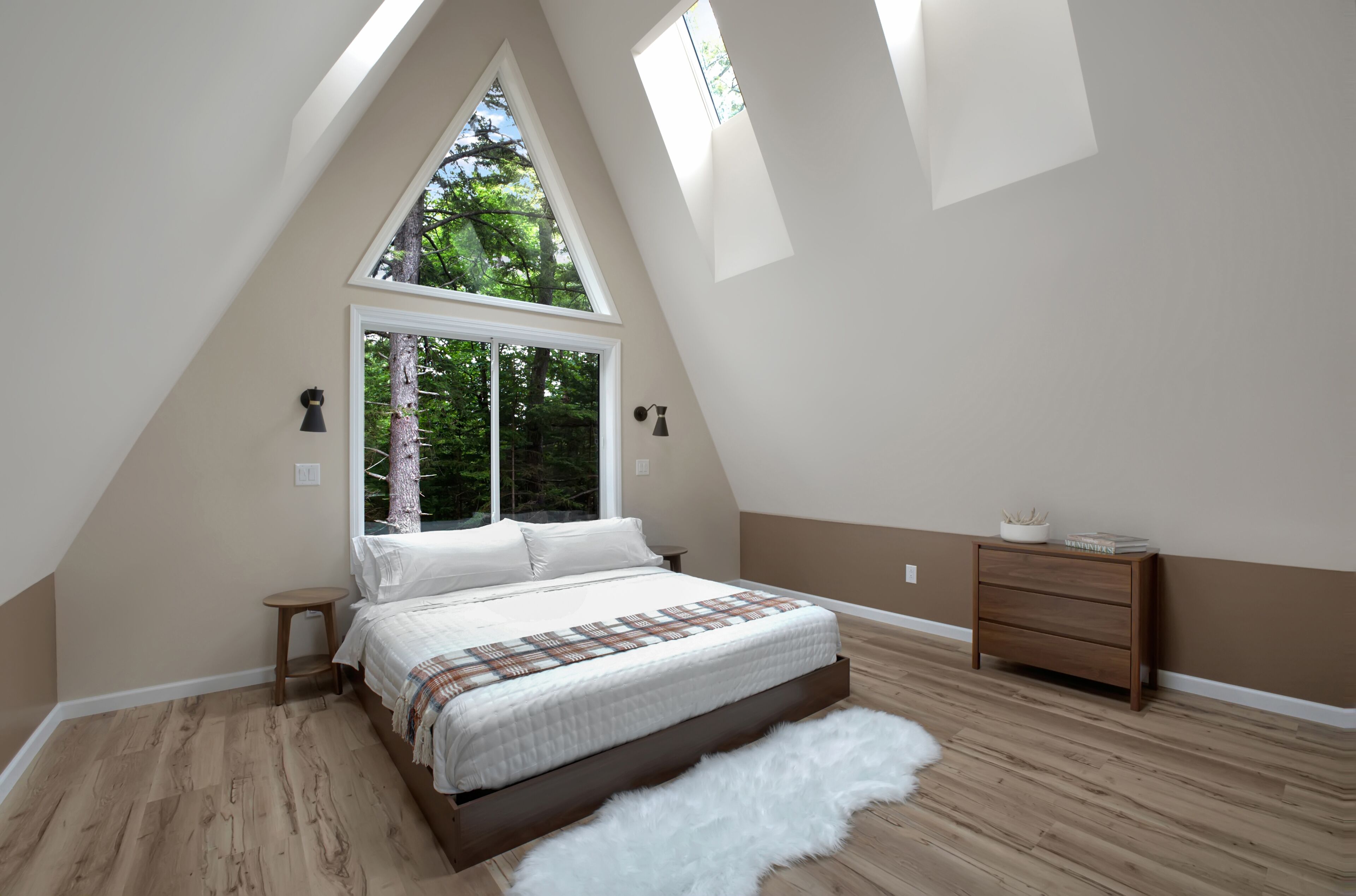 Un dormitorio con techo inclinado, un ventanal grande, una cama, una mesita de noche y un aparador.
