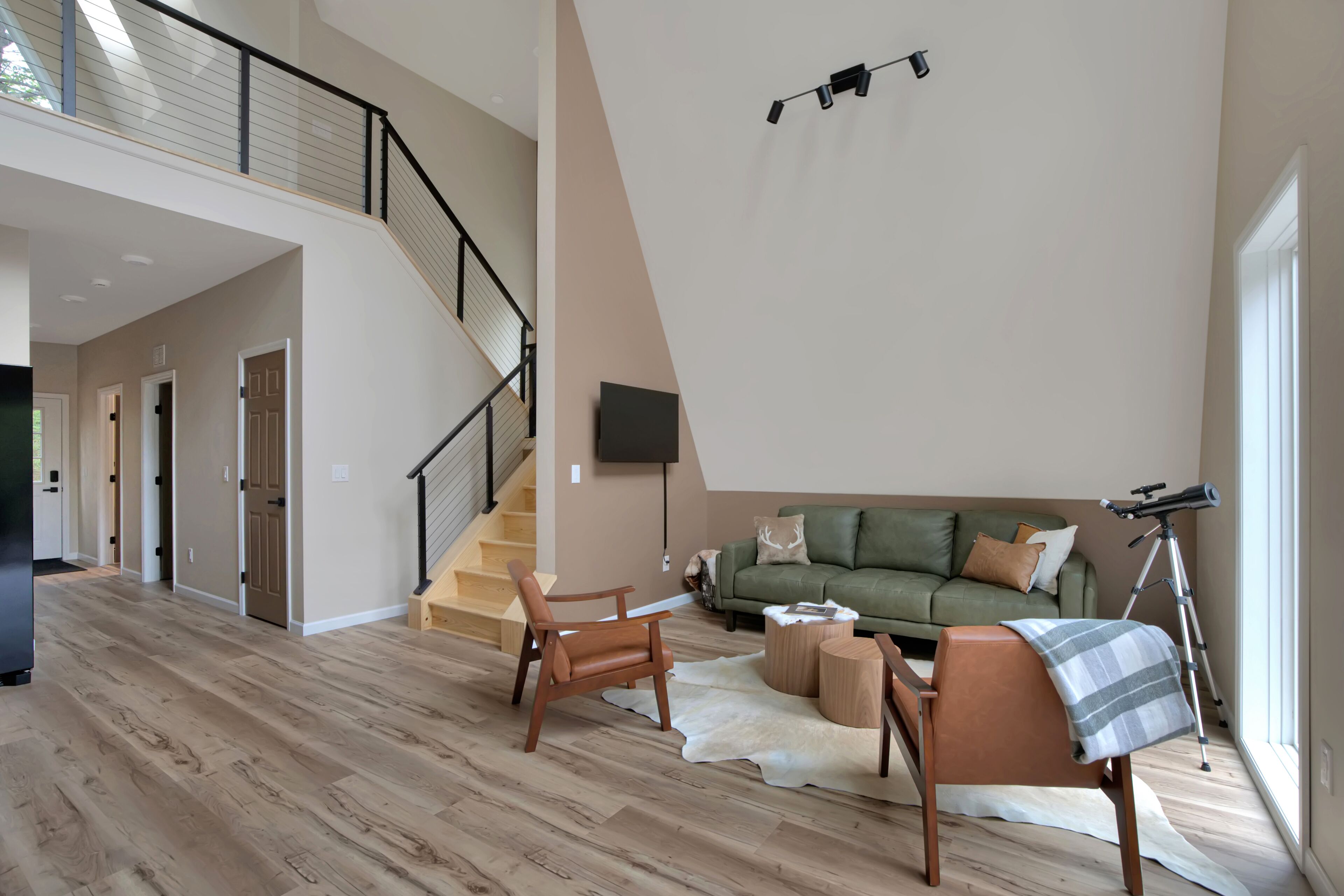 Un vaste espace de vie comprenant un escalier, un canapé vert, un télescope et un plancher en bois.