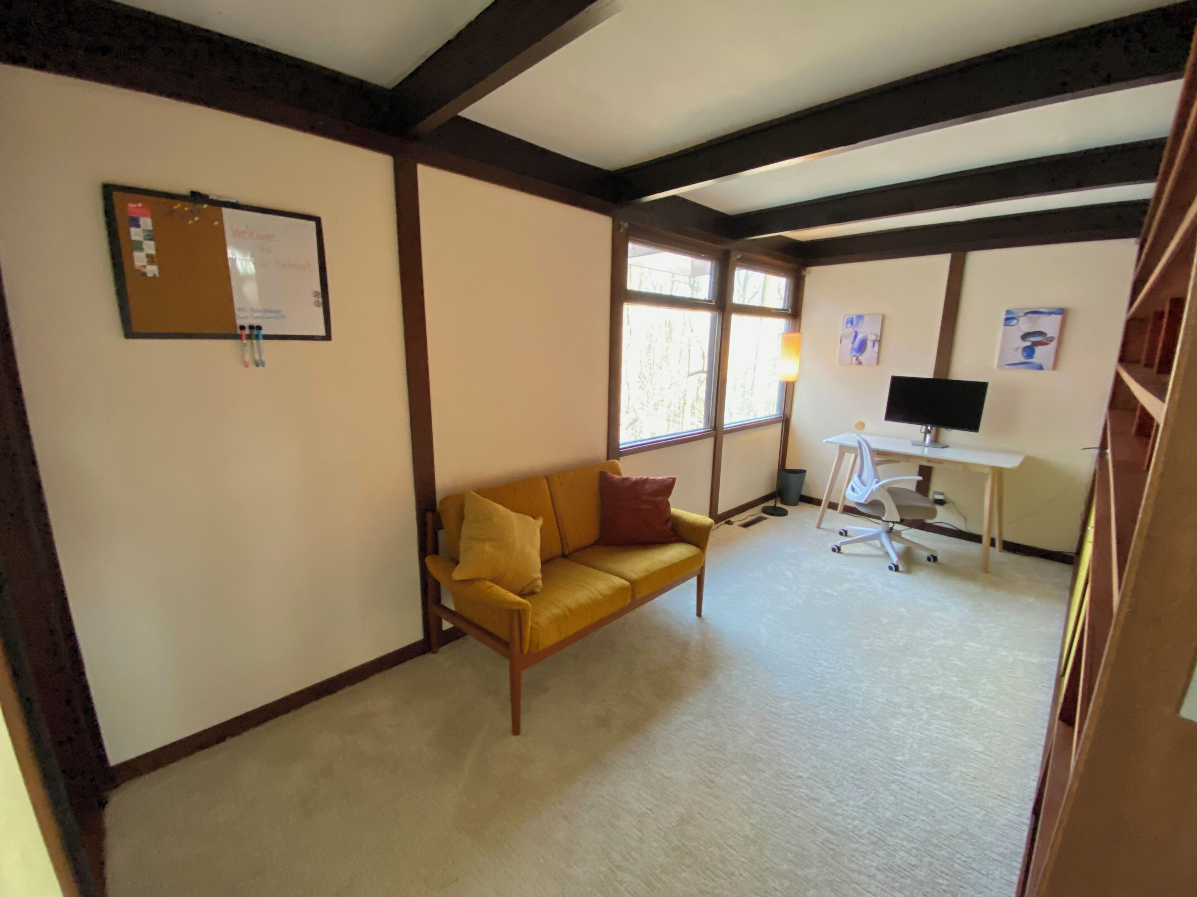 Ein Zimmer mit einem gelben Sofa, einem Schreibtisch mit einem Computer und einem Fenster.
