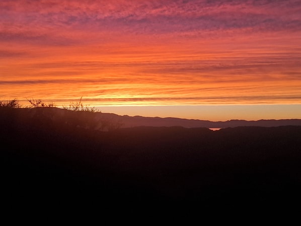 A sunset over a mountainous landscape with silhouettes of vegetation and distant hills.