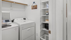 Une buanderie équipée de deux machines à laver et de deux sèche-linge à chargement frontal, d’un étendoir et d’étagères avec des boîtes de rangement, ainsi qu’un panneau suspendu.