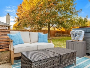 A patio with a sofa, two pillows, a wicker ottoman, and a basket on a grill. - Serene 3-bedroom house with AC in charming McKinney (McKinney)