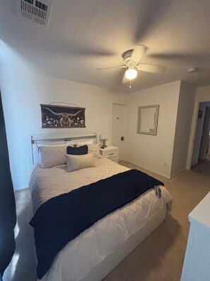 A bedroom with a bed, a nightstand, a ceiling fan, a door, and a wall-mounted mirror. - Serene 3-bedroom house with AC in charming McKinney (McKinney)