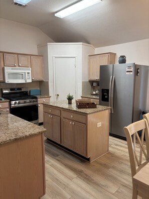 A kitchen with wooden cabinets, a stainless steel refrigerator, a microwave, and a stove. - Serene 3-bedroom house with AC in charming McKinney (McKinney)