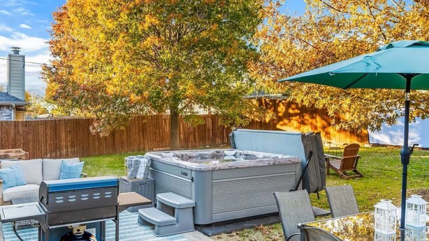Un jardin avec un jacuzzi, du mobilier d’extérieur et une clôture en bois.