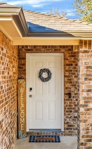 A brick house with a white front door, a welcome mat, and a wreath. - Serene 3-bedroom house with AC in charming McKinney (McKinney)