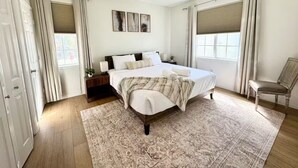 Ein Schlafzimmer mit Bett, Nachttischen, einem Sessel, einem Deckenventilator und einem Fenster mit Vorhängen.