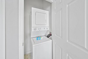 A laundry room with a front-loading washer and dryer, a door, and a small shelf with a Snuggle detergent box. - Sunny escape in Miramar Beach, sleeps 6 (Miramar Beach)