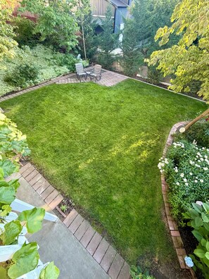 A well-maintained backyard with a lawn, patio furniture, and a brick border. - Unwind in a peaceful private garden retreat just one block from Columbia River. (Richland)