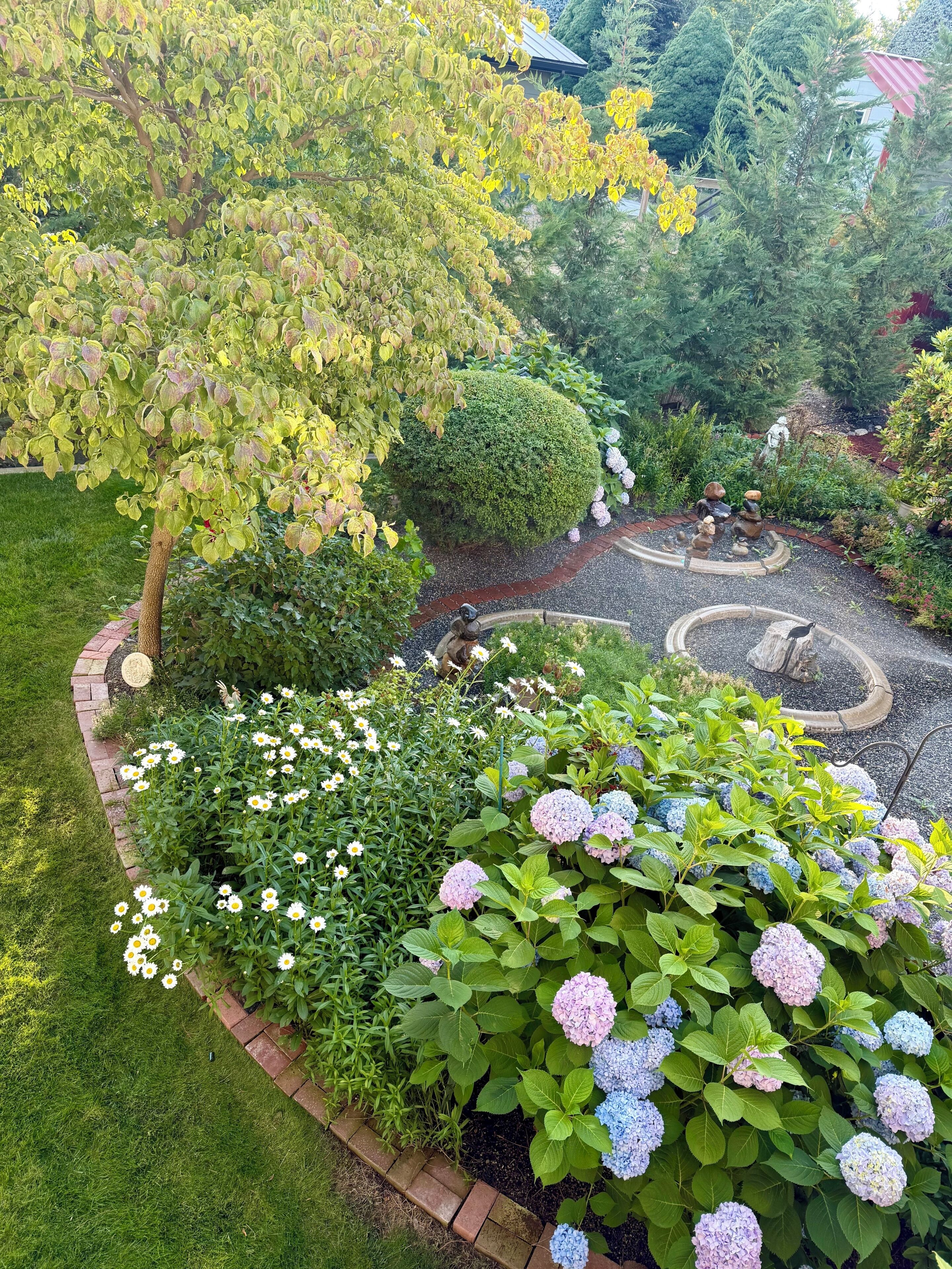 A garden with a variety of plants, a circular stone pathway, and a statue of a bear.