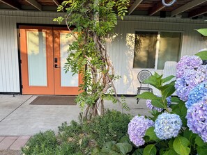 Ein Haus mit einer Holzveranda, einer Glasschiebetür, einer kleinen Au ßenlounge und Hortensienblüten.