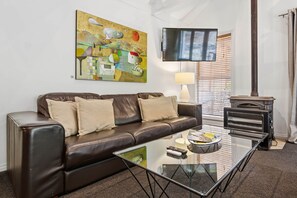 A modern living room with a leather sofa, a glass coffee table, a flat-screen TV, a fireplace, and a large abstract painting.
