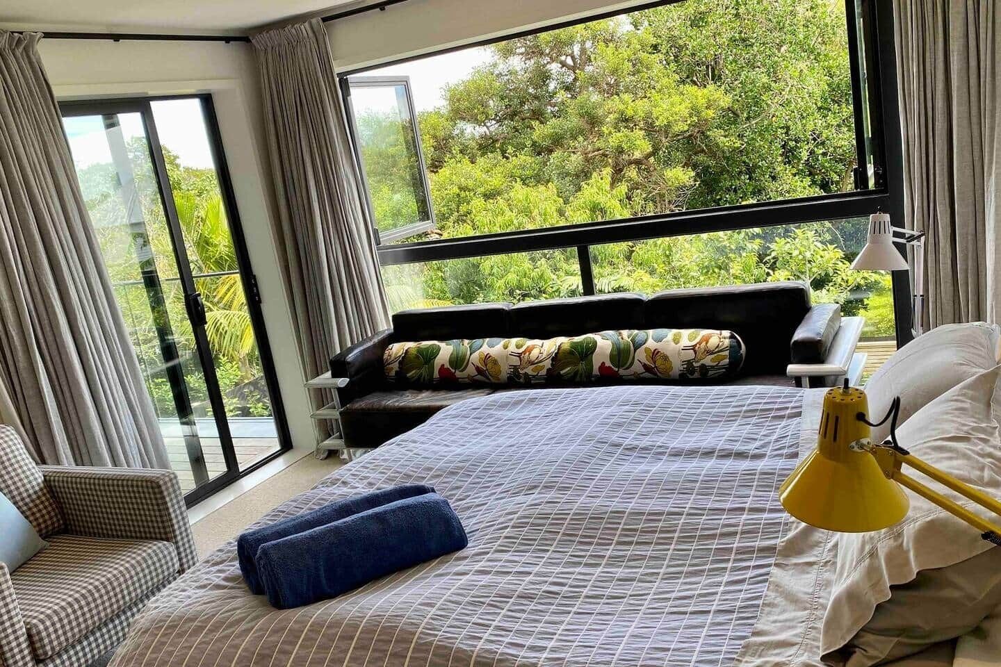 Een slaapkamer met een groot bed, een stoel, een bank en uitzicht op groen door het raam.