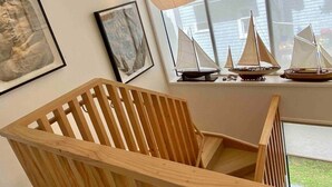 Una sedia di legno in una stanza con una finestra, un quadro incorniciato e un modellino di una barca a vela su uno scaffale.