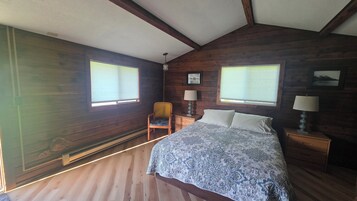A bedroom with a bed, two bedside tables, a chair, and two windows.