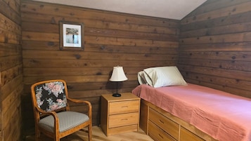 Una habitación de cabaña de madera con una cama, una silla, una mesita de noche y una lámpara.