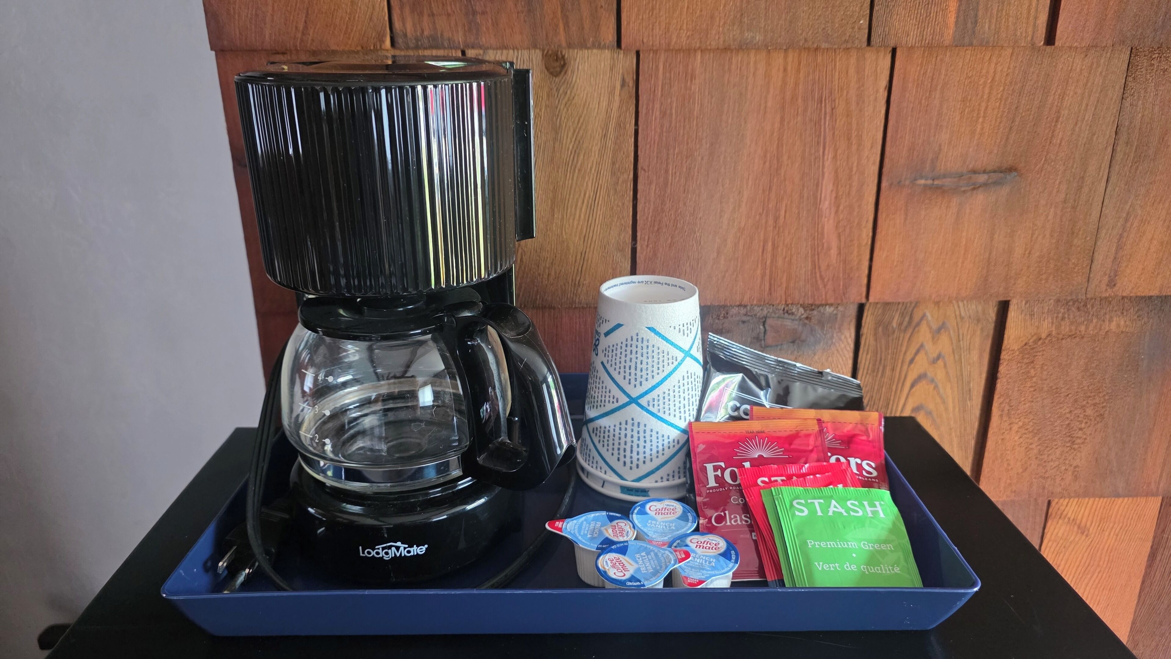 A coffee maker, a paper cup, and coffee pods on a tray.
