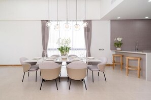 Ein moderner Essbereich mit einem rechteckigen Tisch, sechs Stühlen, Pendelleuchten, einem Fenster mit Vorhängen sowie einer Küchenzeile mit Barhocker.
