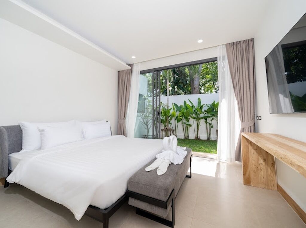 Un dormitorio moderno con una cama grande, un banco de madera y vistas a zonas verdes.