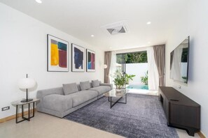 Ein modernes Wohnzimmer mit einem grauen Sofa, einem Couchtisch, einem Fernseher und einem großen Fenster mit Vorhängen.