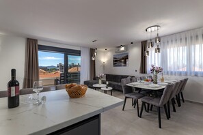 Un'area pranzo moderna con un piano di lavoro in marmo, tavolo, sedie e vista sugli edifici attraverso ampie finestre.