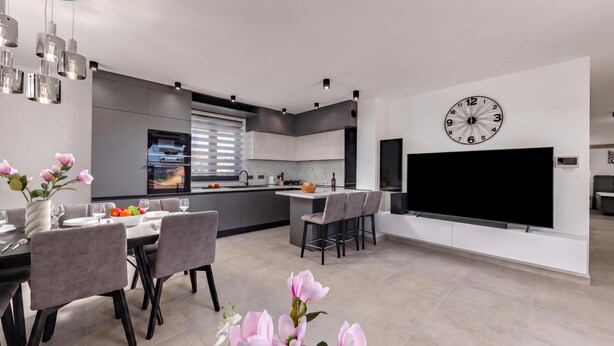 A modern kitchen with a large island, dining area with chairs, a flat-screen TV, and a clock on the wall. - Zadar 3BR Penthouse /w Rooftop Terrace & Jacuzzi, Zadar, Croatia (Zadar)