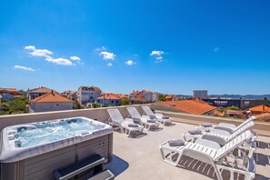 Eine Dachterrasse mit Whirlpool und Liegestühlen mit Blick auf ein Wohngebiet mit roten Ziegeldächern.