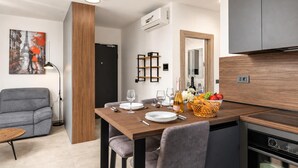 Een moderne eetruimte met een houten tafel gedekt voor vier personen, een grijze bank en een keuken met een inbouwoven.