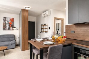 Ein moderner Essbereich mit einem Holztisch, gedeckt für vier Personen, einer grauen Couch und einer Küche mit Einbauofen.