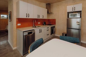 Une cuisine compacte avec des meubles blancs, un réfrigérateur en acier inoxydable, un four à micro-ondes et un lave-vaisselle. On y trouve une table à manger avec deux chaises.