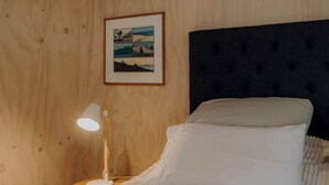 Ein ordentlich bezogenes Bett mit weißen Leinen, ein dunkles Kopfbrett und ein gerahmtes Bild an der Wand.