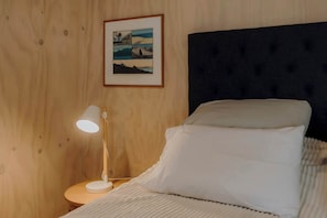 Ein ordentlich bezogenes Bett mit weißen Leinen, ein dunkles Kopfbrett und ein gerahmtes Bild an der Wand.