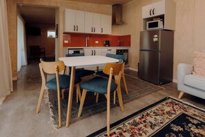 A compact kitchen with a dining table, chairs, a refrigerator, and a microwave. - Tremorne Stay: Couples Retreat in Taranaki (Inglewood)