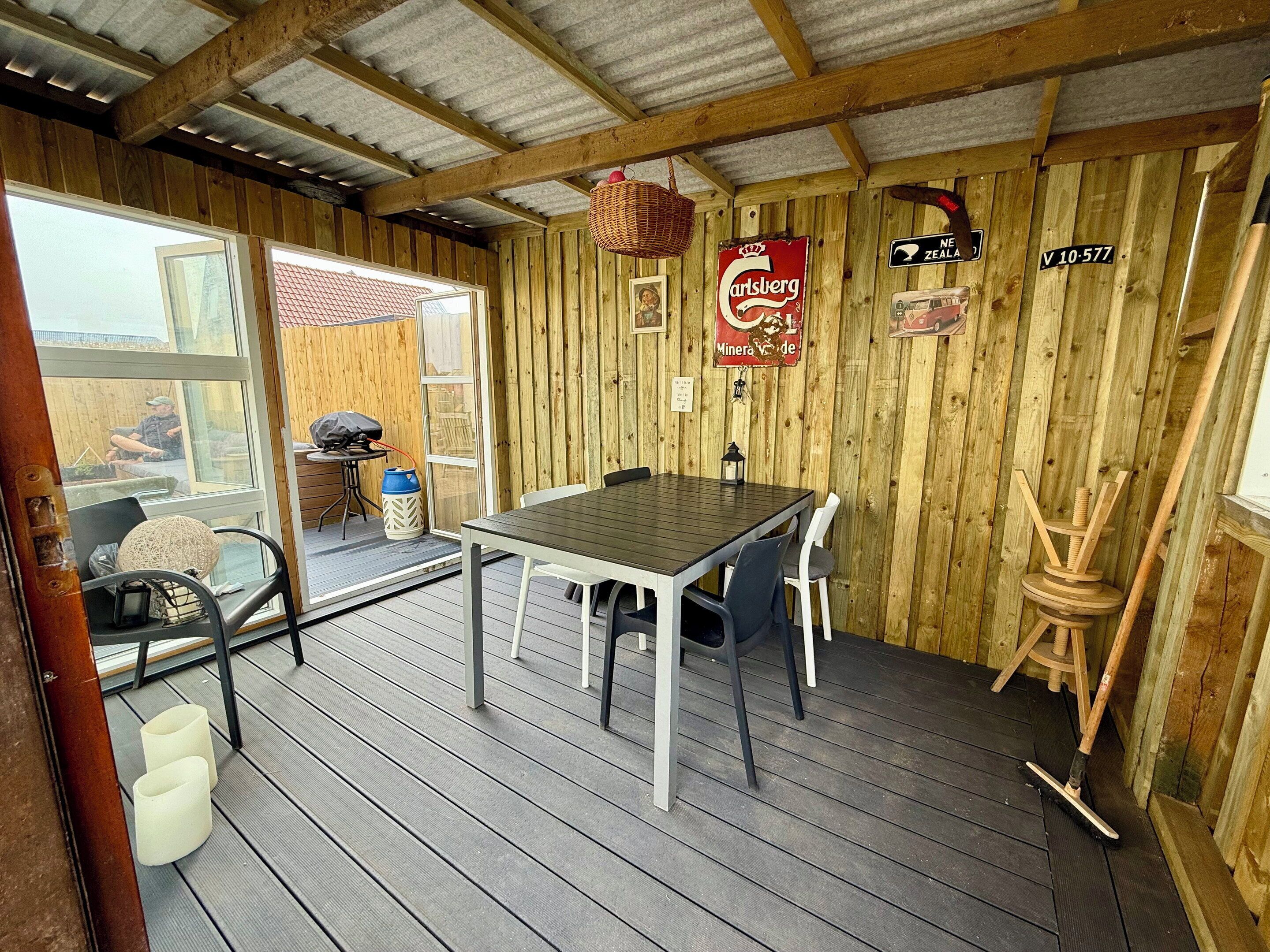 A wooden interior with a table and chairs, a wicker basket, and a sign indicating a New Zealand location.