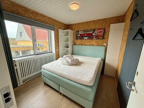 Ein Schlafzimmer mit einem Bett, einem Heizkörper, einem Fenster und einem Wandregal.