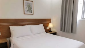 A neatly made bed with white linens, a wooden headboard, a bedside lamp, and a framed plant on the wall. - HOTEL LUXURY DREAM (Bogotá)