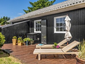 Une maison en bois noire, dotée d’une terrasse, d’une porte coulissante et d’une fenêtre.