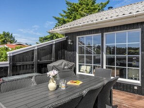 Une terrasse avec une table, des chaises, un barbecue couvert et une grande fenêtre.
