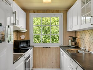 A compact kitchen with white cabinetry, a built-in oven, a microwave, and a window with a view of greenery. - "Isabel" - 650m from the sea by Interhome (Løkken)